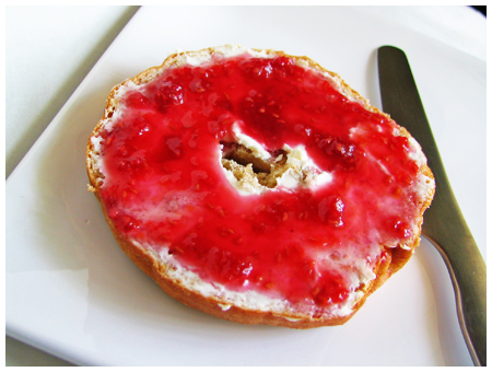 raspberry sauce drizzled over whipped cream cheese schmeared honey wheat bagel